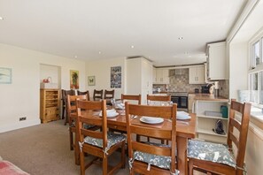 A dining area with a wooden table and chairs, a kitchen in the background, and a window with a view. - Ghyllstead - North East Escapes (Glanton)