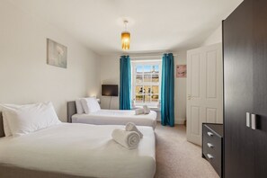 Una habitación de hotel con dos camas, un escritorio, un televisor, un armario y una ventana con cortinas.