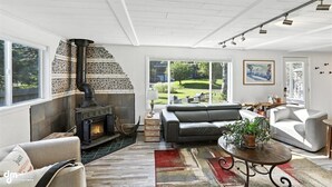 A spacious living room with a stone fireplace, leather sofas, and a large window overlooking a garden. - Once a 1950s Alaska Railroad Section House, this unique home blends modern comfort with vintage soul (Anchorage)