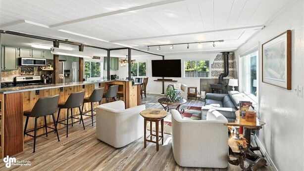 A modern open-plan living area with a kitchen, bar seating, and a large TV. - Once a 1950s Alaska Railroad Section House, this unique home blends modern comfort with vintage soul (Anchorage)