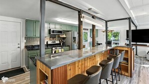 A modern kitchen with a central island, green cabinets, and a large TV. - Once a 1950s Alaska Railroad Section House, this unique home blends modern comfort with vintage soul (Anchorage)