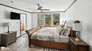 A bedroom with a wooden bed, a ceiling fan, a window with blinds, a TV mounted on the wall, and a nightstand with a lamp. - Once a 1950s Alaska Railroad Section House, this unique home blends modern comfort with vintage soul (Anchorage)