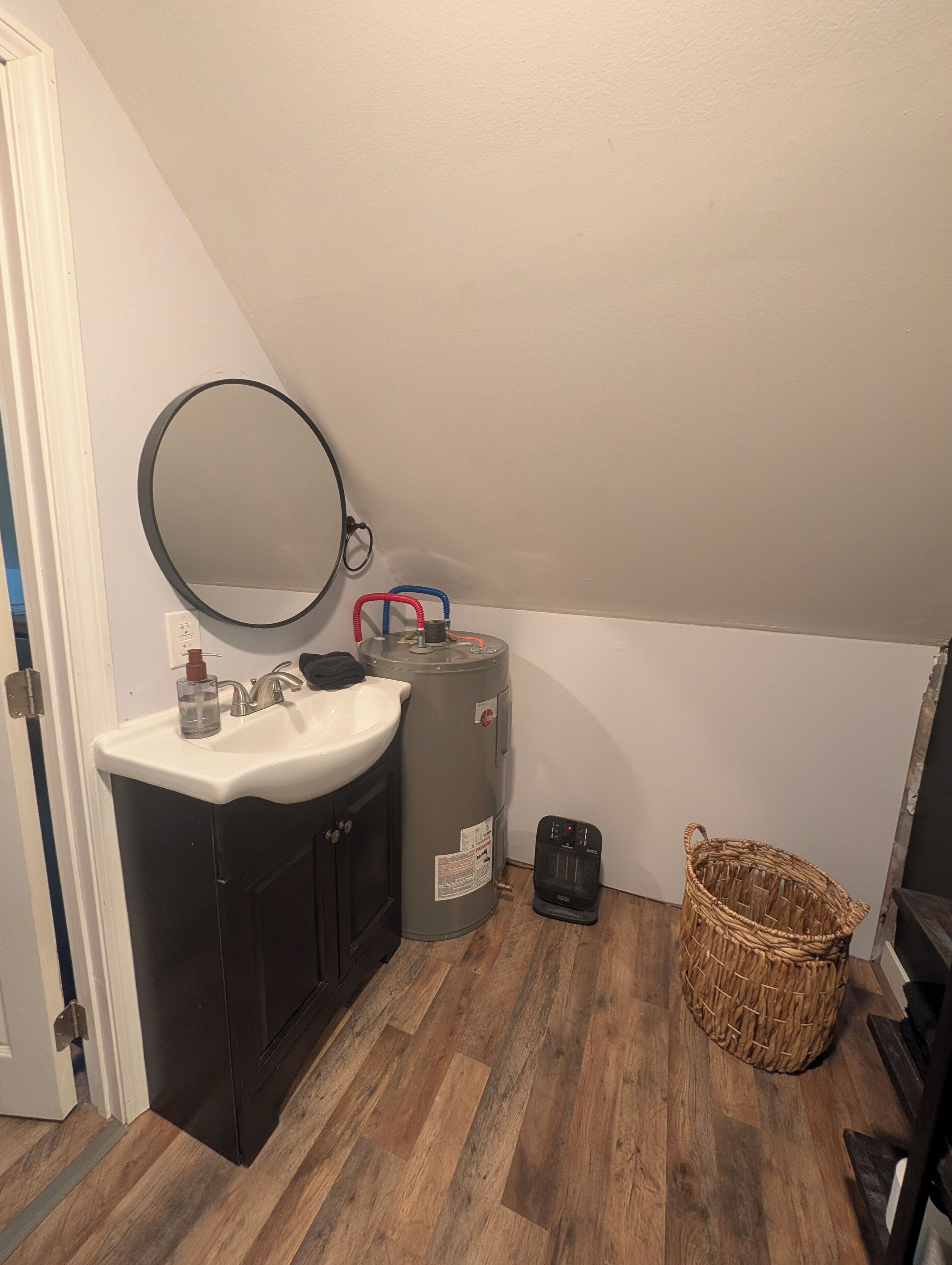 Ein Badezimmer mit Waschbecken, Spiegel, Heizung und einem Korbwäscheschrank.