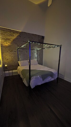 Un lit à baldaquin décoré de guirlandes lumineuses, un mur en briques et un plancher en bois.