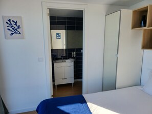 Un dormitorio con cama, armario, baño con lavamanos y espejo, y una pared con un cuadro abstracto azul.