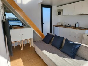 A compact living space with a sofa, a kitchenette, and a view of the water. - Barco Casa Aveiro (Aveiro)