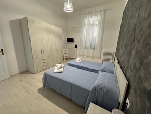 A bedroom with two beds, a wardrobe, a chair, a radiator, and a TV on the wall.