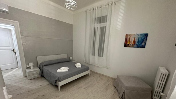 A bedroom with a bed, bedside table, lamp, curtains, a radiator, and a painting on the wall. - Casa Pinuccio Sapri: Bike-Friendly Holiday Home Steps from the Sea (Sapri)