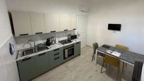 A compact kitchen with a sink, stove, microwave, and a dining area with a table and chairs. - Casa Pinuccio Sapri: Bike-Friendly Holiday Home Steps from the Sea (Sapri)