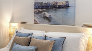 Ein Schlafzimmer mit einem Bett, Kissen, einem Wandbild mit einer Küstenansicht und Nachttischlampen.