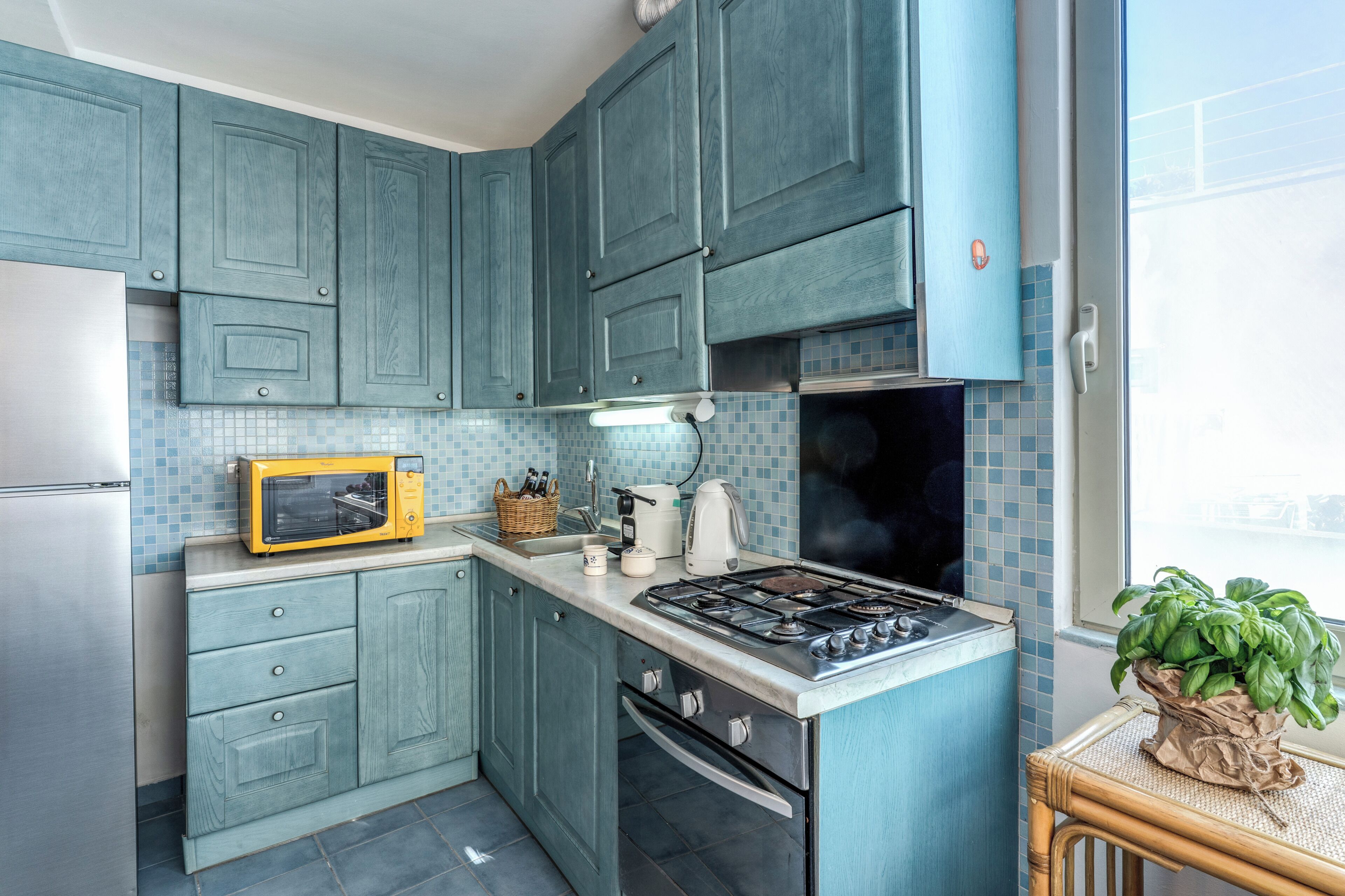 Une cuisine avec des meubles de couleur turquoise, un four à micro-ondes, une cuisinière et une fenêtre donnant sur un beau paysage.