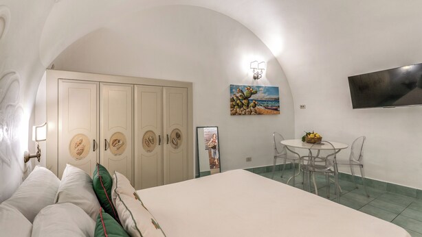 A bedroom with a bed, a desk with chairs, a television, and a painting on the wall. - Lapuritate Via Cariddi - Monolocale piano terra (Gallipoli)