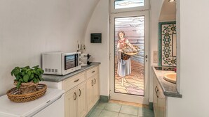 A kitchen with a microwave, a basket with plants, and a door with a stained glass design. - Lapuritate Via Cariddi - Monolocale piano terra (Gallipoli)