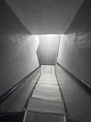 A narrow, dimly lit stairwell with a metal handrail and wooden steps. - Amazing 5-bedroom house in quaint Cleveland perfect for your stay (Cleveland)
