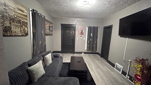 Moderni olohuone, jossa on sohva, sohvapöytä, taulutelevisio ja taideteoksia seinillä.
