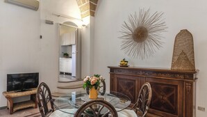 Un comedor con mesa de vidrio, sillas de mimbre, un armario de madera y un televisor sobre un mueble.