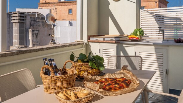 Terraza en la azotea con una mesa lista para comer, que incluye un cesto de pan, una pizza y botellas.