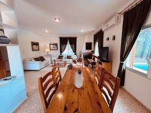 A dining area with a wooden table, chairs, and a vase of dried flowers. There is a sofa and a television in the background. - La Rincona House, Chulilla (Chulilla)