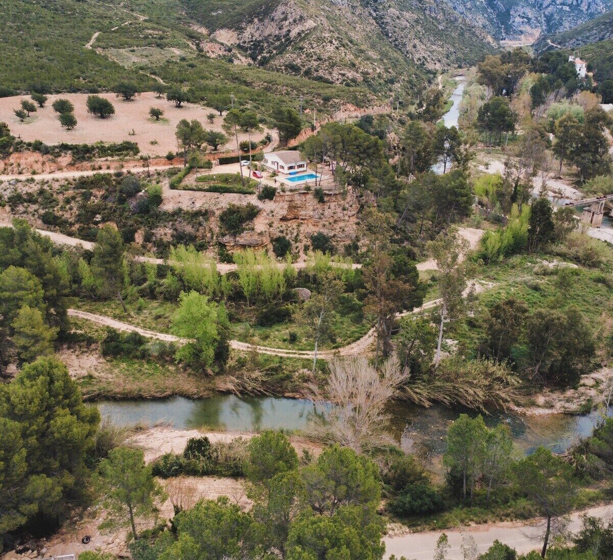 A mountainous landscape with a house, a swimming pool, and a river.