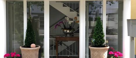 A glass door entrance with a staircase leading to an upper floor, potted plants, and a metal railing.