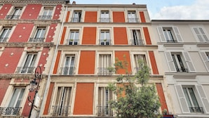Un edificio de varios pisos con fachadas de ladrillo rojo, contraventanas blancas y balcones con barandillas de hierro forjado.
