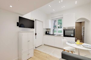 Una cocina moderna con armarios blancos, horno empotrado, televisor y comedor con mesa y sillas.