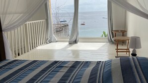 A bedroom with a large bed, a view of the sea, and a balcony with a railing. - The House on the Beach (Saint-Pierre)