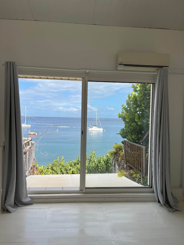 A room with a large sliding glass door leading to a balcony overlooking a marina with boats and a clear sky. - The House on the Beach (Saint-Pierre)