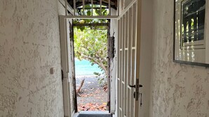 A hallway with a tiled floor leading to an open door with a view of a garden. - The House on the Beach (Saint-Pierre)