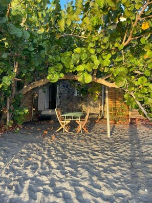 A covered outdoor seating area with a table and chairs, surrounded by foliage. - The House on the Beach (Saint-Pierre)