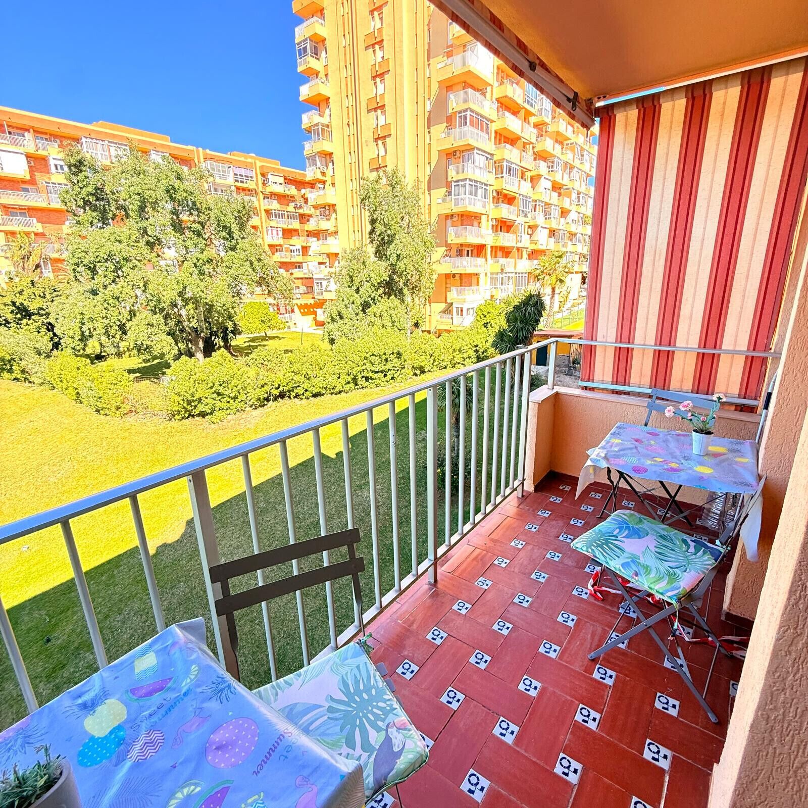 Un balcon avec une table et des chaises, une vue sur un quartier résidentiel et un rideau rouge.