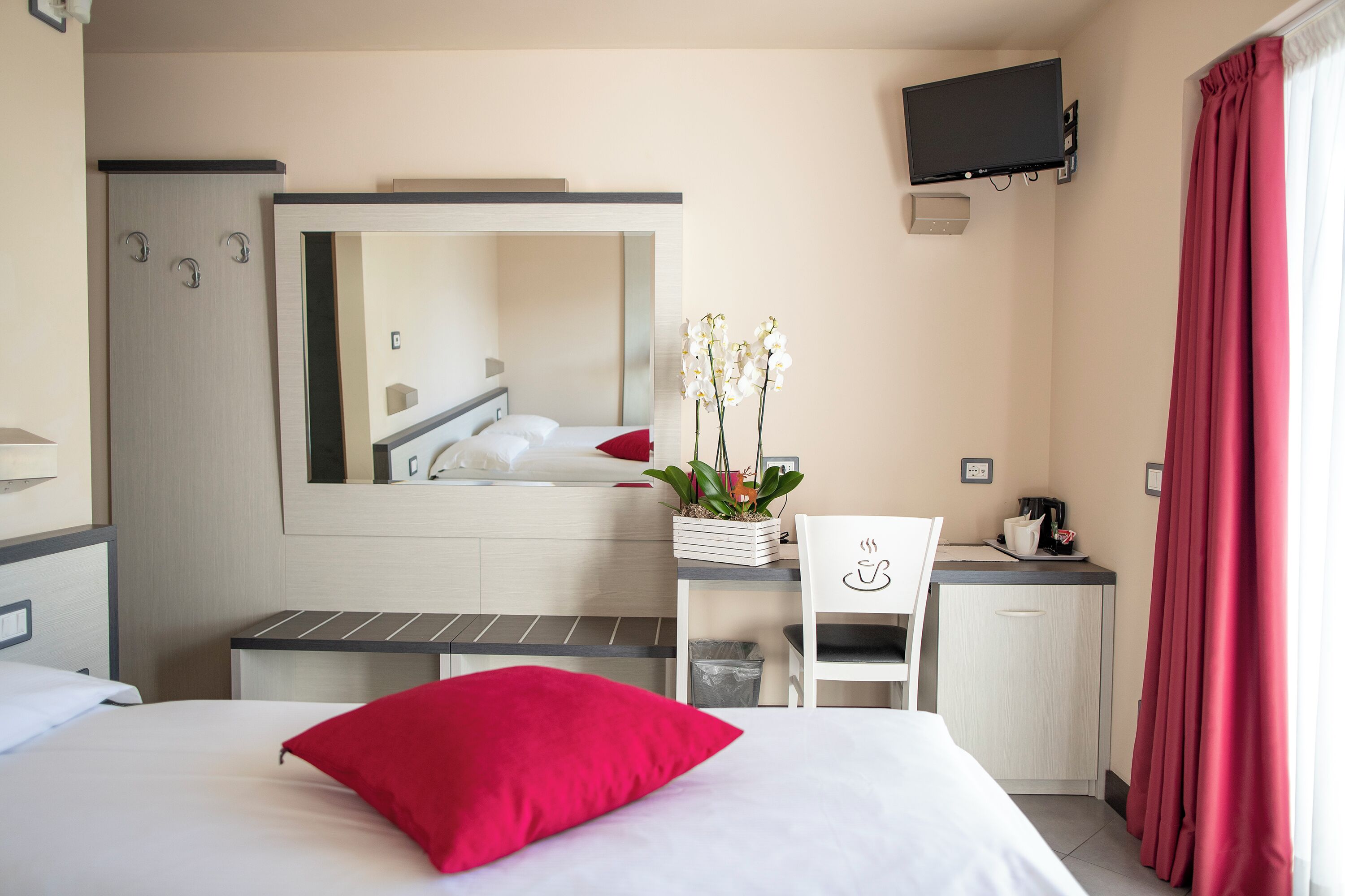 A hotel room with a bed, a desk, a chair, a TV, and a mirror.