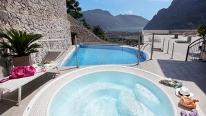 A hot tub with a view of mountains and a pool area with lounge chairs and a stone wall. - Acetaia del Balsamico Trentino (Tenno)