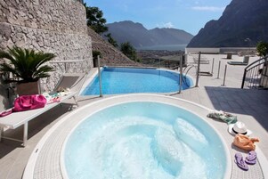 Un jacuzzi con vistas a montañas y un área de piscina con sillas de descanso y un muro de piedra.