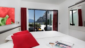 A hotel room with a bed, red pillows, a magazine, and a view of mountains through a sliding door. - Acetaia del Balsamico Trentino (Tenno)