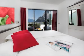 A hotel room with a bed, red pillows, a magazine, and a view of mountains through a sliding door.
