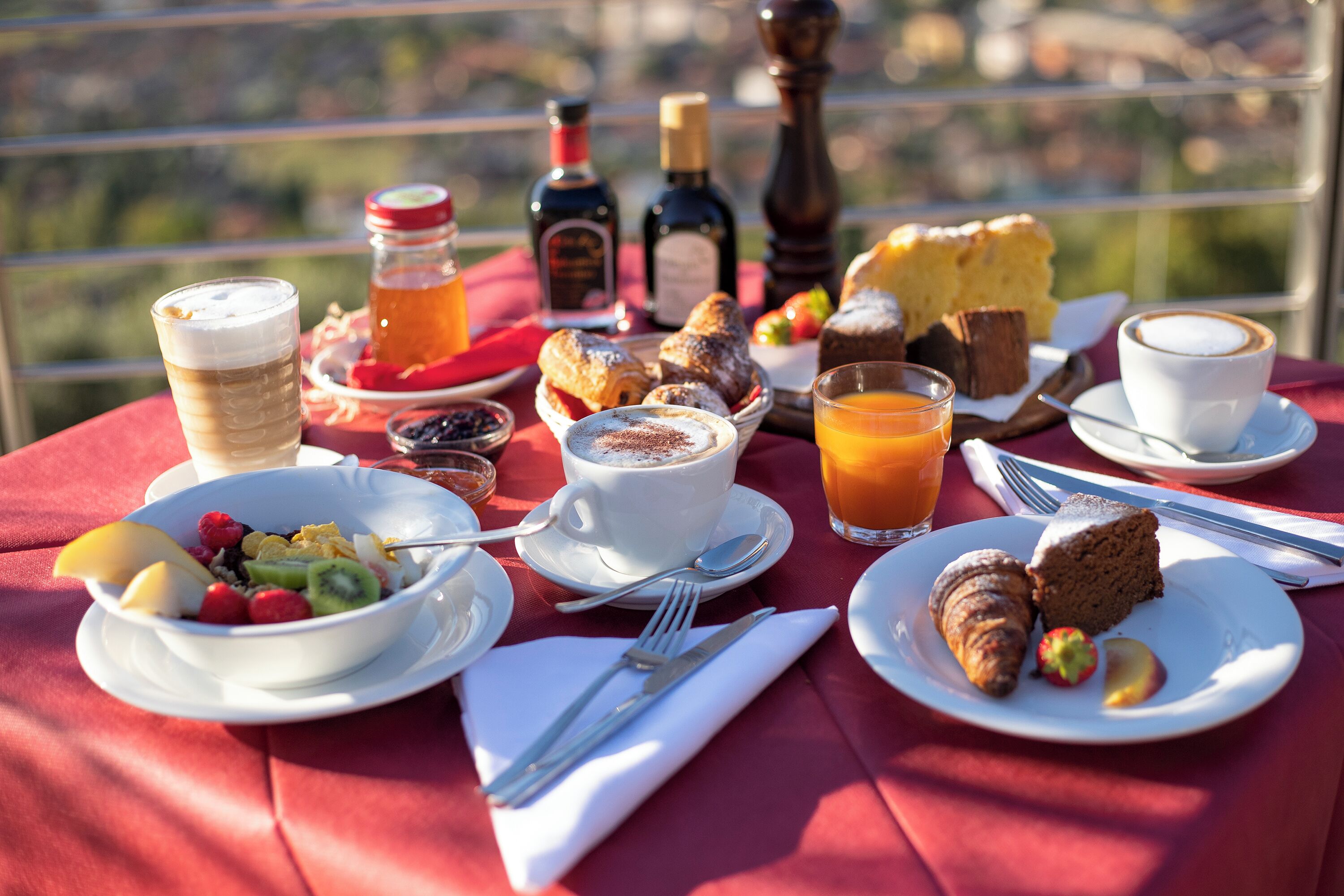 A table set with breakfast items including croissants, pastries, fruit, and beverages, with a scenic view in the background.