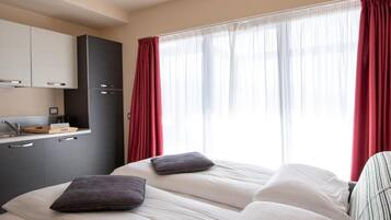 Une chambre d’hôtel équipée d’un lit, d’une télévision, d’une kitchenette et d’une fenêtre avec des rideaux.