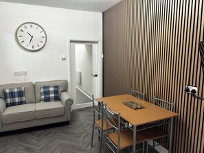 A modern living room with a sofa, a dining table, a clock, and a wooden panel wall. - 2 bedroom house in central swansea (Swansea)