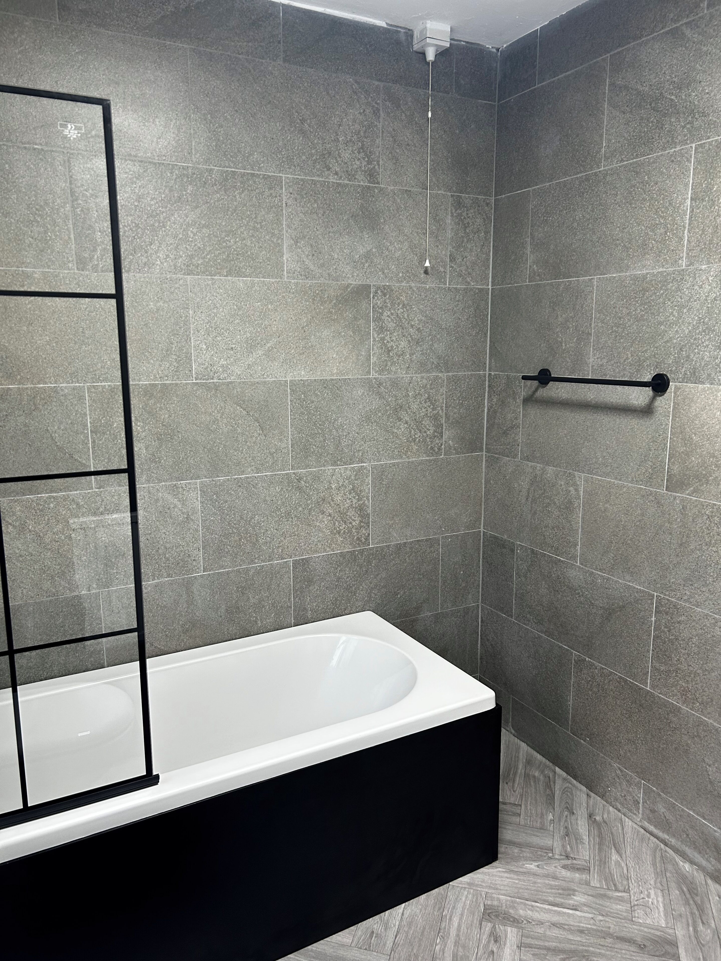 Une salle de bain moderne avec une baignoire rectangulaire, un porte-serviettes noir et un miroir fixé au mur.