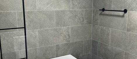 Une salle de bain moderne avec une baignoire rectangulaire, un porte-serviettes noir et un miroir fixé au mur.