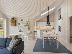 Ein geräumiges Wohnzimmer mit einer Couch, einer Essecke mit Tisch und Stühlen, einer Küche mit weißen Schränken und einer Decke mit Holzlatten.