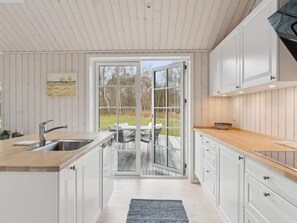 Eine moderne K üche mit weißen Schränken, einer Holzausziehtafel, einem Edelstahlspülbecken und einer Glastür zu einer Terrasse.