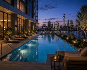 A rooftop pool with lounge chairs and a view of a city skyline at dusk. - KL Gateway Residences by Bangsar (Kuala Lumpur)