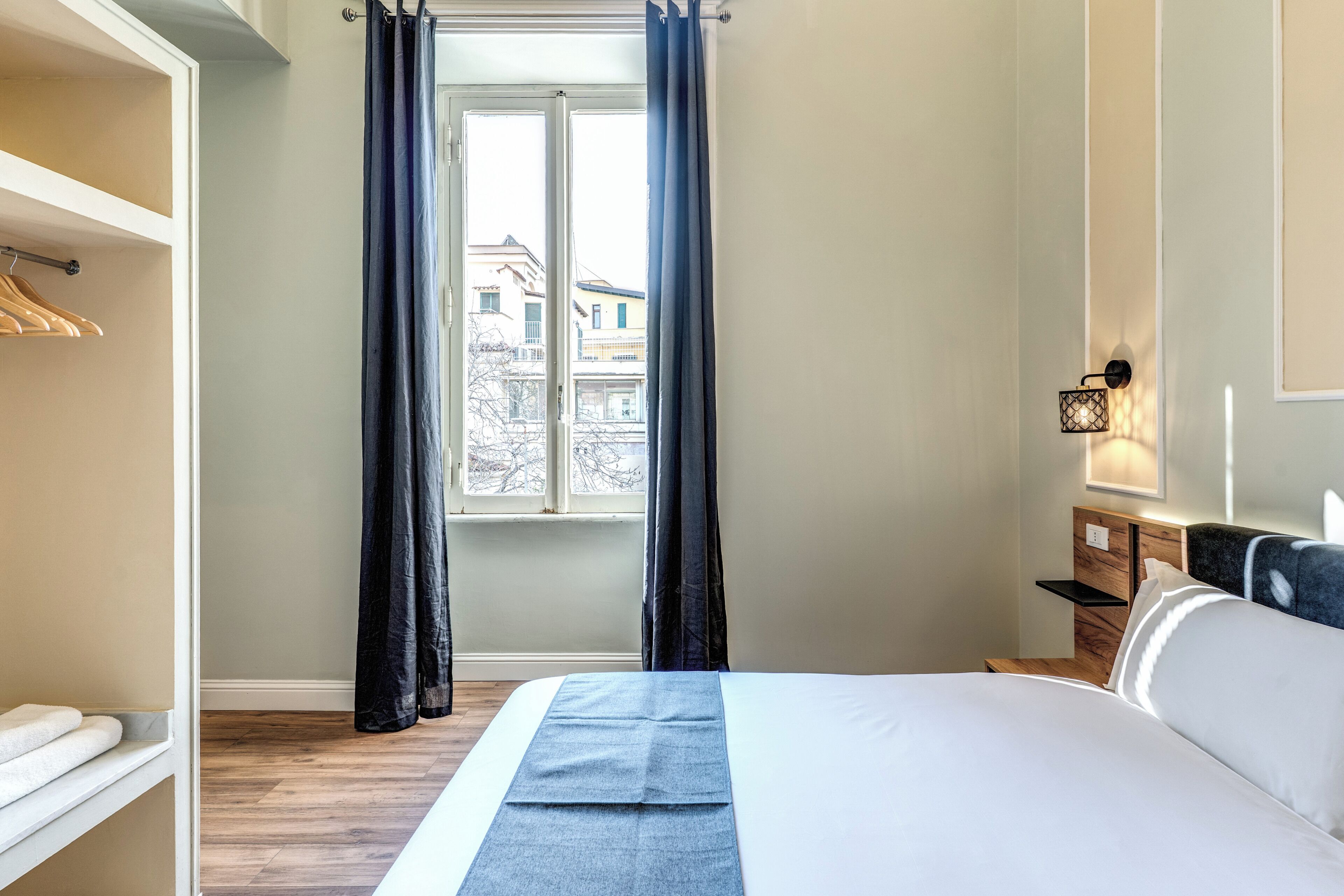 Un dormitorio con cama, mesita de noche, armario y ventana con cortinas.