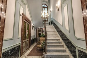 A grand staircase with a chandelier, a chair, and a door with a sign. - Venere's Villa (Roma)
