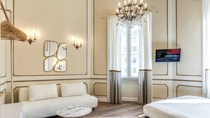 A hotel room with a sofa, a bed, a TV, a chandelier, and a window with curtains. - Venere's Villa in Rome (Roma)