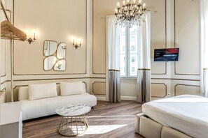 A hotel room with a sofa, a bed, a TV, a chandelier, and a window with curtains. - Venere's Villa (Roma)