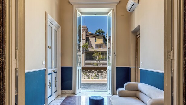 A hallway leading to a balcony with a sofa and ottoman, a door with a nameplate, and a view of buildings. - Venere's Villa in Rome (Roma)