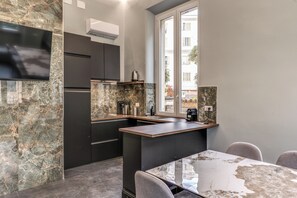 A modern kitchen with dark cabinetry, a marble backsplash, and a large window. - Venere's Villa (Roma)